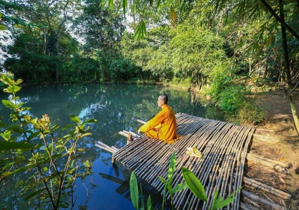 A person sitting on a bamboo bridge over a body of water

Description automatically generated