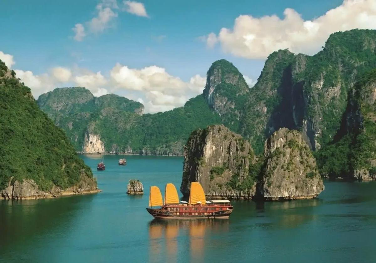 A boat in the water with mountains in the background with Ha Long Bay in the background

Description automatically generated