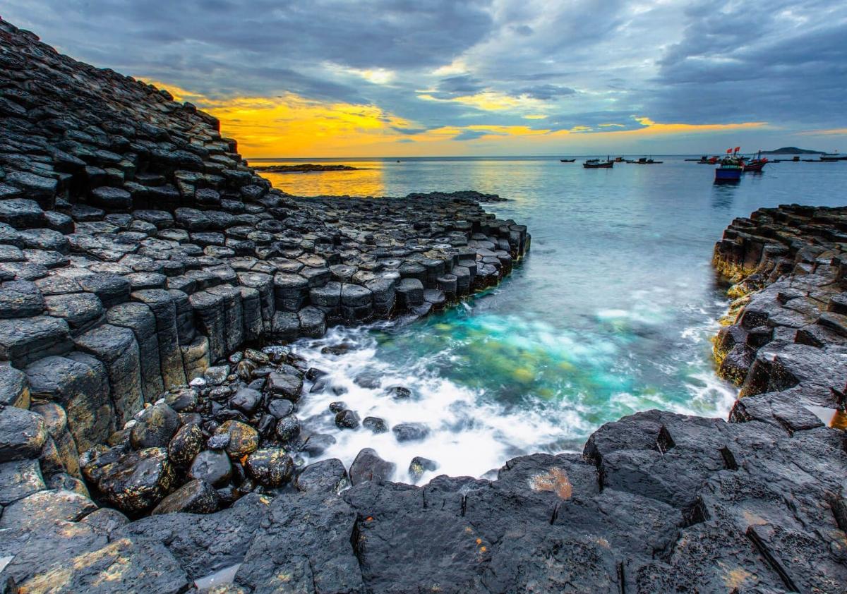 A rocky shore with a body of water and boats

Description automatically generated