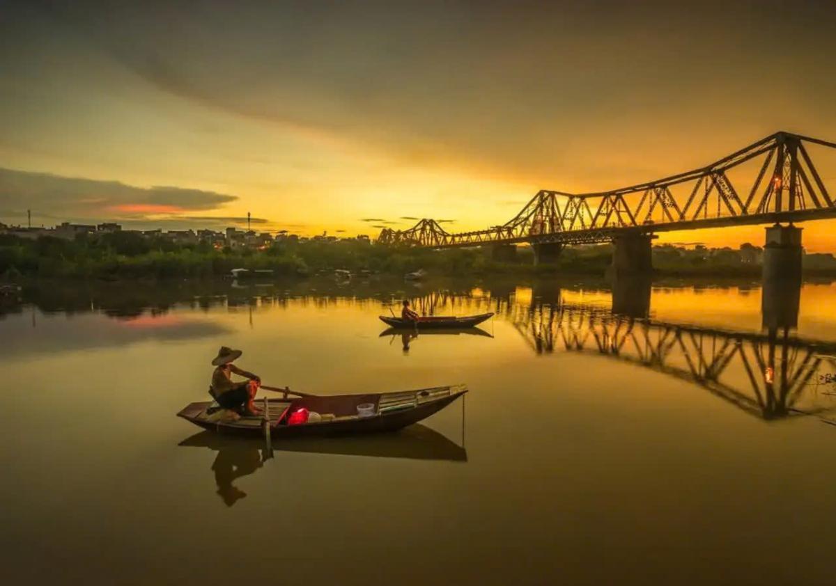 A couple of people rowing boats on a river with a bridge in the background

Description automatically generated