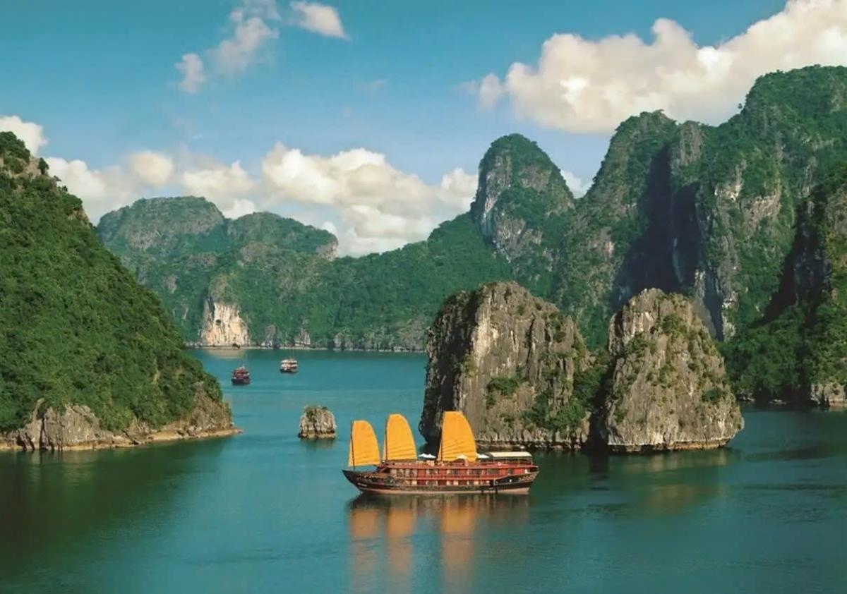 A boat in the water with mountains in the background with Ha Long Bay in the background

Description automatically generated