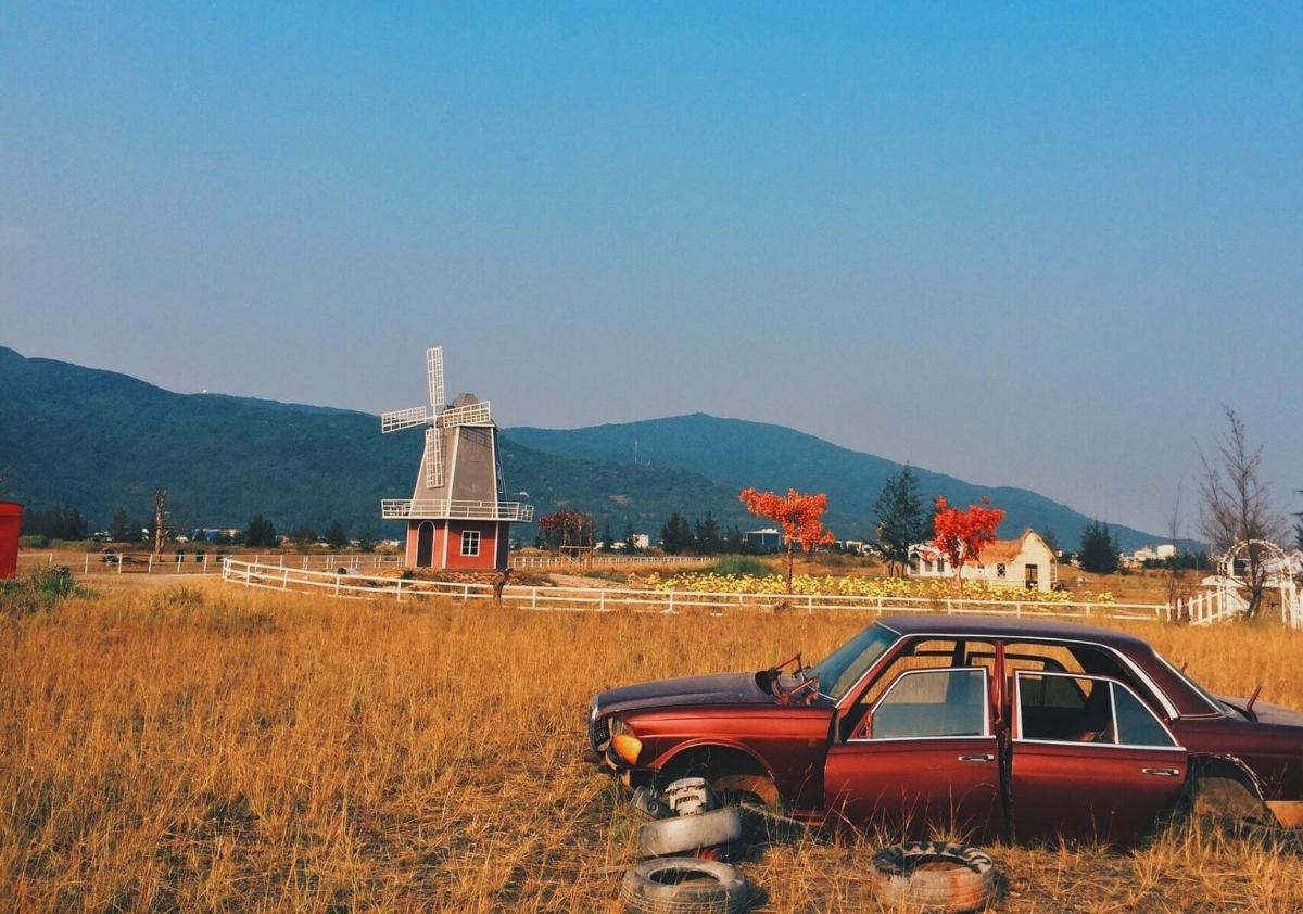 A car in a field with a windmill in the backgroundDescription automatically generated