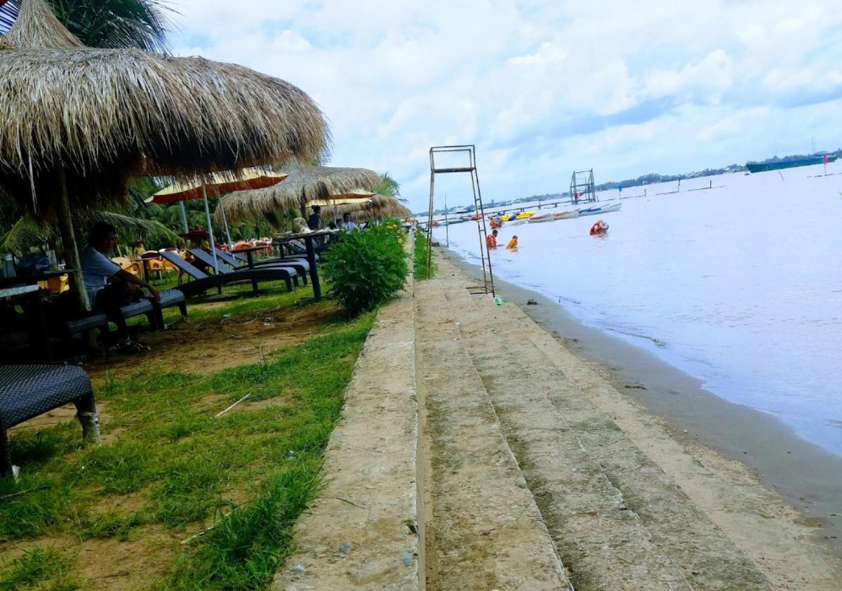 A beach with a thatched umbrella and chairsDescription automatically generated