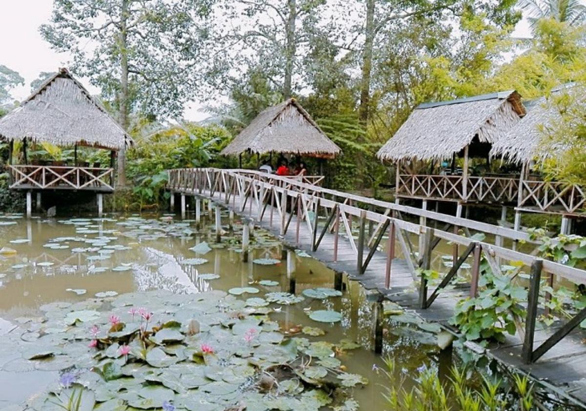 A bridge over water with huts and a pondDescription automatically generated